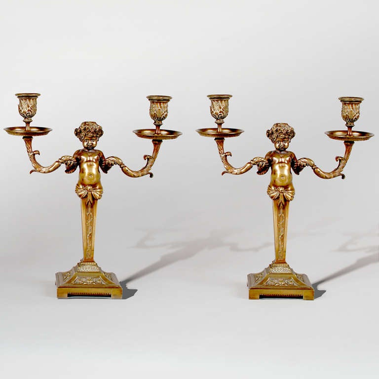 Pair of gilt bronze candelabra featuring robust putti figures, arms extended. Swags support candleholder cups.