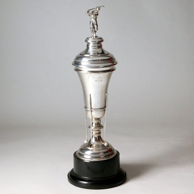 Elegant sterling silver English golfers trophy raised on separate black base. Removable lid topped with golfer swinging club, dressed in period tennis costume. Vase-shaped trophy held upright with golf club supports. Hallmarked: Birmingham, England,