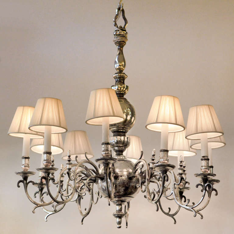 Silver plated ten-light chandelier with scrolled branches arranged in a single tier around a central baluster column ending in a large globe-shaped pendant.
