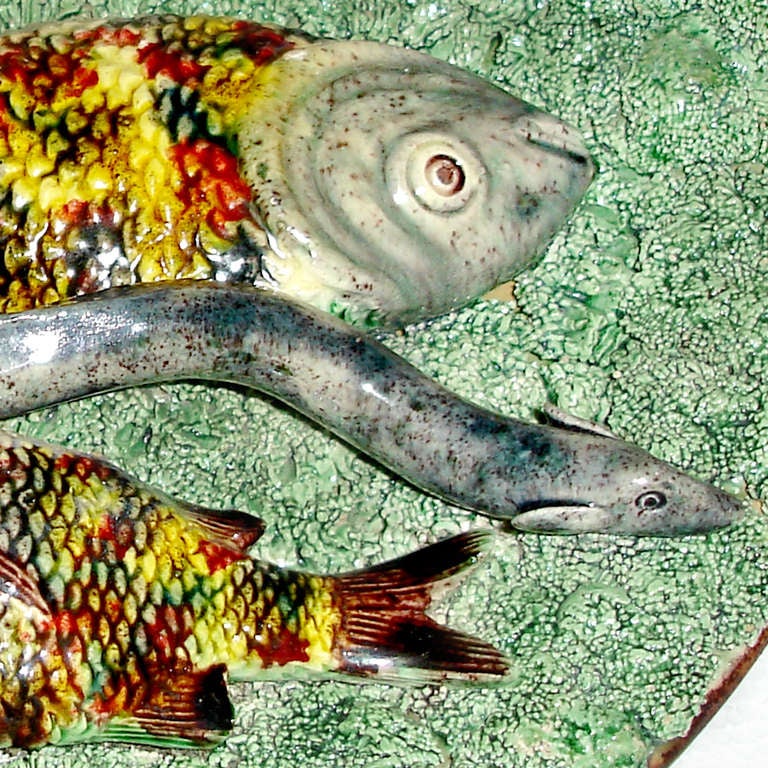 Late 19th century Portuguese palissy plate with green grass background and three colorful fish in yellow, brown and red with a single grey-black eel between them. Impressed: M. Mafra, Caldas, Portugal.