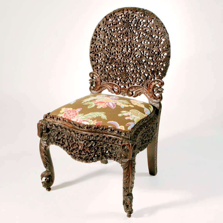 Set of four matching oval back Burmese side chairs intricately carved in an interlocking floral pattern with a scrolled leaf on the lower chair back, a raised carved seat edge, a large carved apron front, all on cabriole front legs ending with an