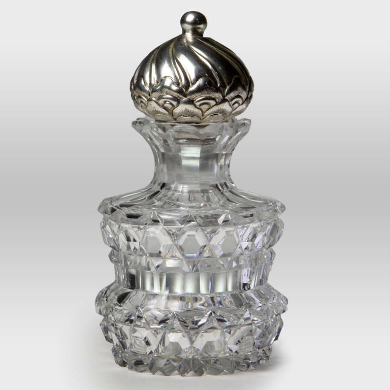 Antique heavy-weight cut crystal perfume bottle with embossed sterling silver top. Bottle body uniquely and deeply cut with rare scalloped edge top. Heavy glass stopper crowned with ornamental turret-shaped sterling silver cover. Hallmarked.