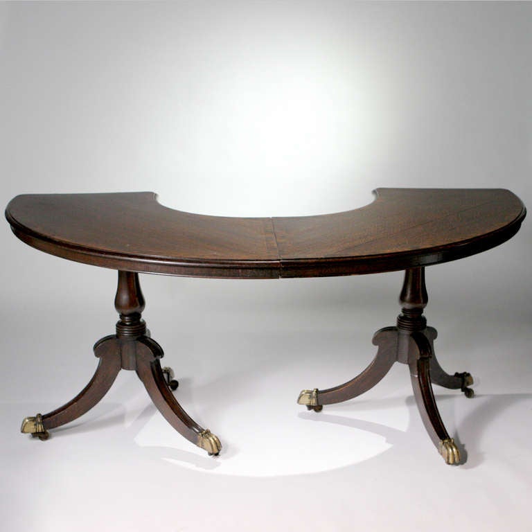 A hard-to-find 19th century English oak hunt table. Demilune shaped table designed as two free-standing pieces that lock together to form one table. Each side supported by a pedestal base and brass covered paw feet on casters.