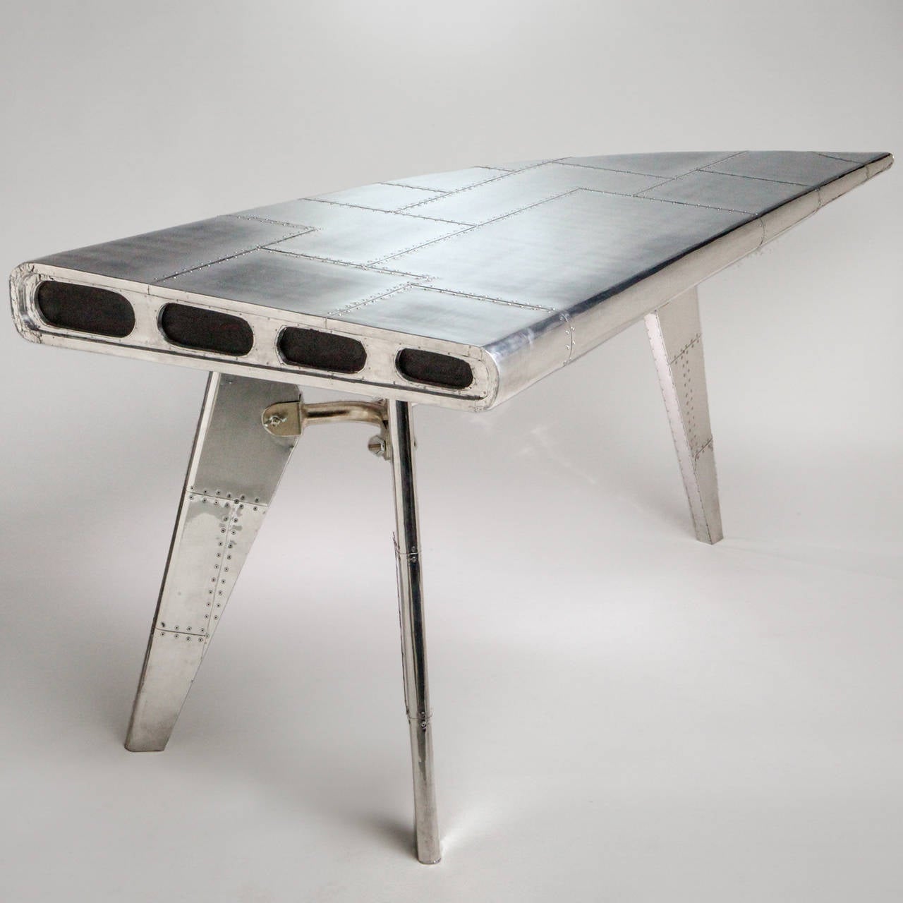 Unique 21st century desk designed as the extended piece of an aluminum riveted airplane wing. On three metal strut shaped legs.