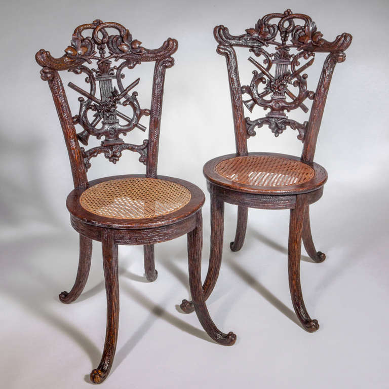 Pair of carved Black Forest oak chairs with round caned seats. Designed with a hunting motif of rustic leaves and hunting horns.