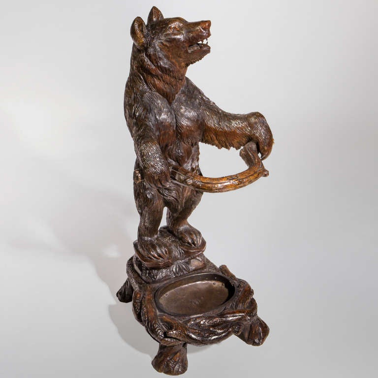 Carved Black Forest bear stick stand in the form of a standing bear perched on a rocky base with paws outstretched to hold a curved branch. Strong depth of character face with roaring expression and traditional glass eyes, stained red tongue and