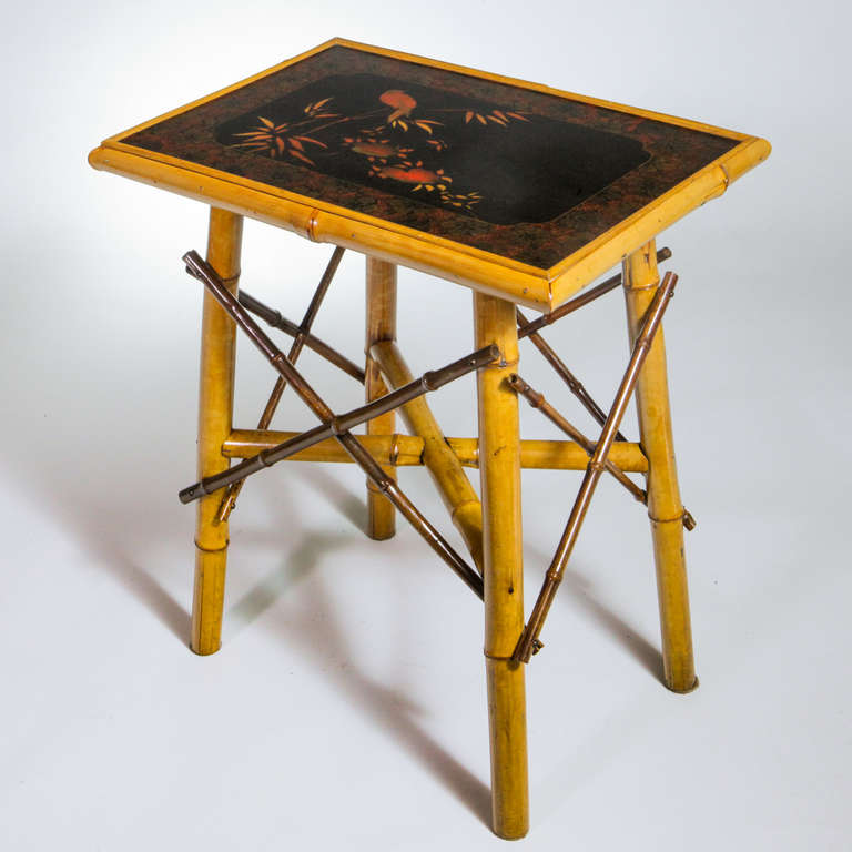 English bamboo end table featuring distinctive darker bamboo side stretchers.  Rectangular shape decorated with Oriental floral and bird motif painted in traditional black, gold and orange chinoiserie.