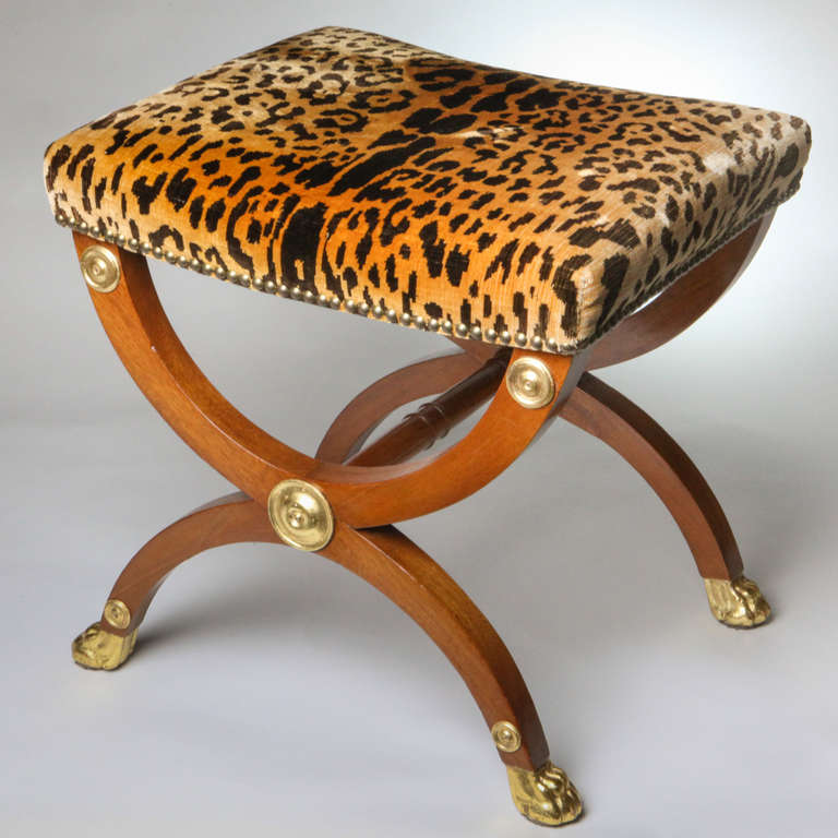 Regency style cross-framed or Curule, bench with fruitwood frame appointed with parcel gilt medallions and paw feet. The seat upholstered with vintage French faux leopard print fabric.