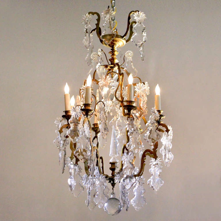 French bronze and crystal chandelier with eight lights on double-scrolled arms ornamented with flat, angular cut crystal drops and twelve-point stars. Interior features a faceted crystal spire. The fixture is surmounted by a tier of branches holding
