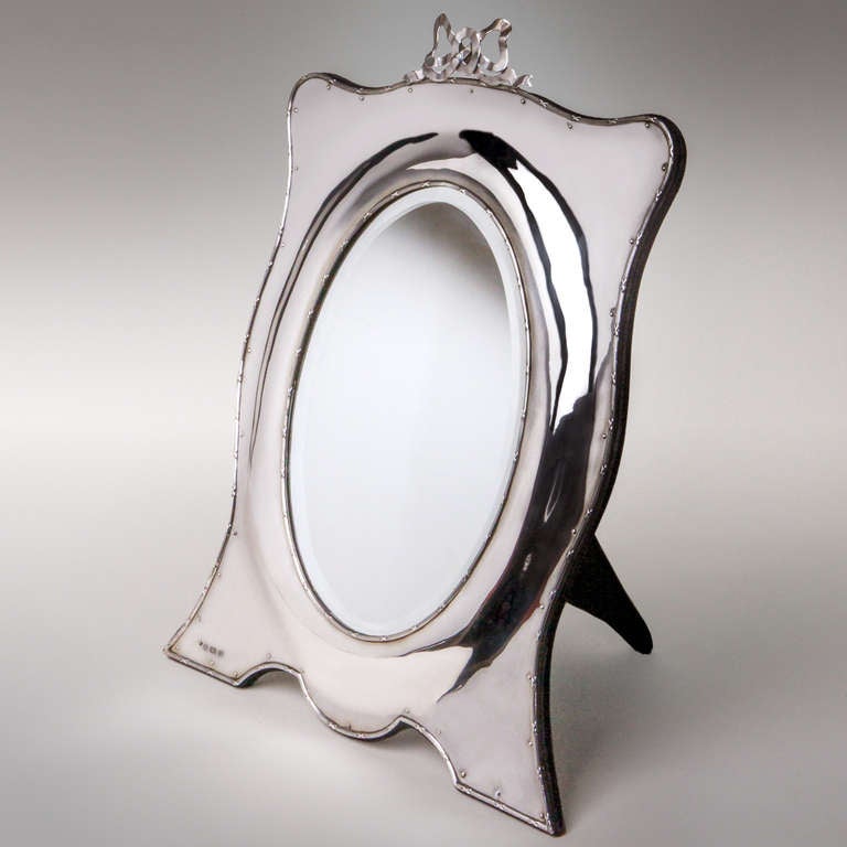 Classic silver dressing table mirror in bowed oval shape with beveled glass, reed wrapped edge and large silver bow on top. Hallmarked: Birmingham, 1904.