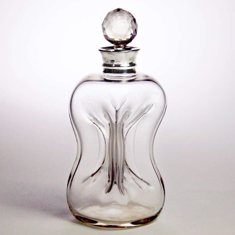 Edwardian Asprey silver mounted glass decanter in pinched cruciform design that was created for easy gripping.  The facetted crystal stopper set in a hallmarked silver neck impressed:  Asprey, London.