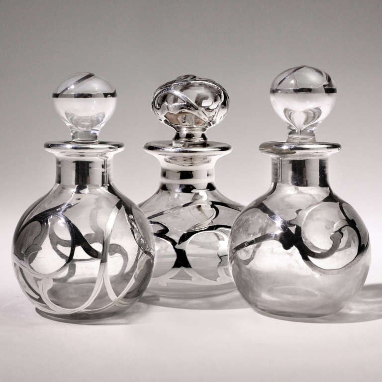 Set of three small Art Nouveau perfume bottle in glass with silver overlay.  Chased silver with flower and vine pattern.  Matching glass stoppers with silver detail.