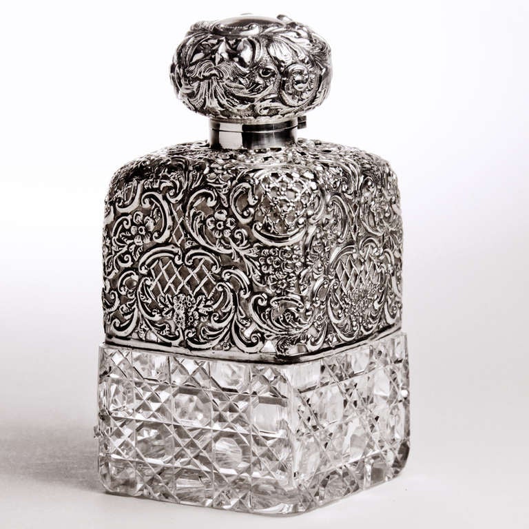 Important Edwardian cut crystal decanter with hallmarked sterling silver top and crystal stopper.  The sterling overlay embossed with cartouches of lattice work with swirling flowers and leaves.  Hidden in the design of the silver cap the face of a