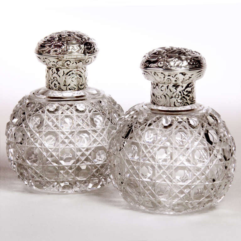 Beautiful pair of English 19th century cut crystal perfume bottles in rare oval shape. The cut crystal in button and daisy pattern, the repousse silver tops with flower and leaf design. Hinge opens to reveal cut crystal stoppers. Hallmarked: Stuart