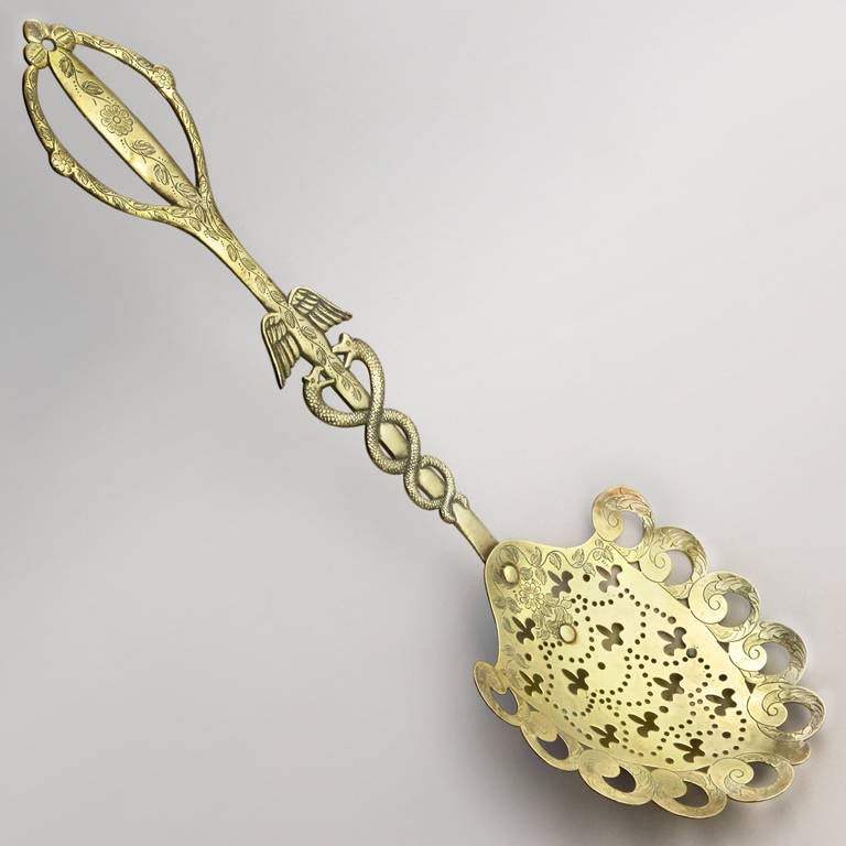 19th century English brass skimmer tool used to remove the solids from the broth. Designed with a fleur de lis pattern bowl and medical symbol or caduceus on the handle.