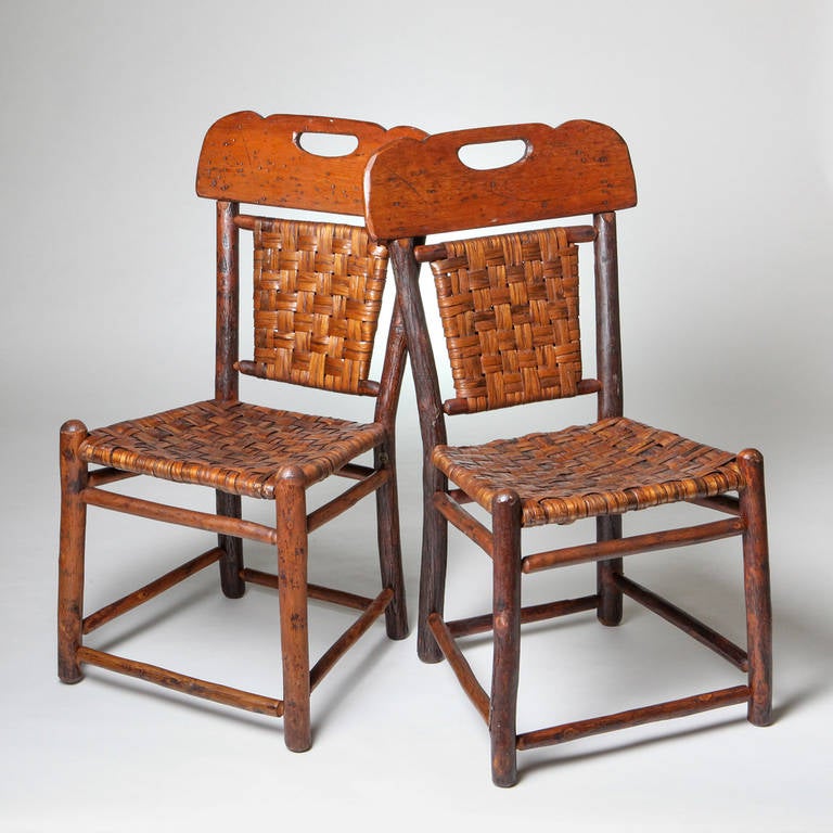 Unique pair of handcrafted antique Old Hickory chairs with carved wood backs and wide woven pealed wood seats. Stamped: Old Hickory, Martinsville, Indiana. Stamped and also has metal plaque with product number.