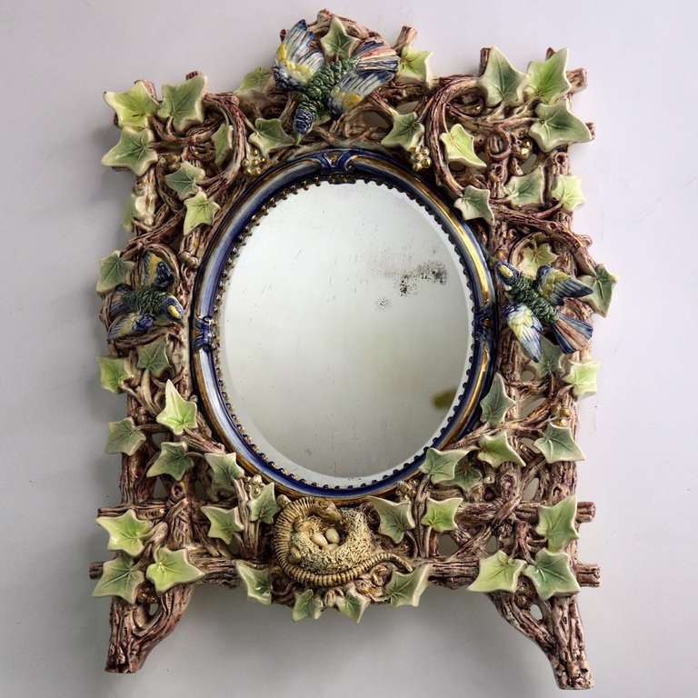 Majolica style pottery mirror in a Black Forest design. The twig frame surrounds an oval mirror with signs of nature, the crown with a large bird, the base with a nest with three eggs and a salamander figure, decorated with touches of gold gilt to