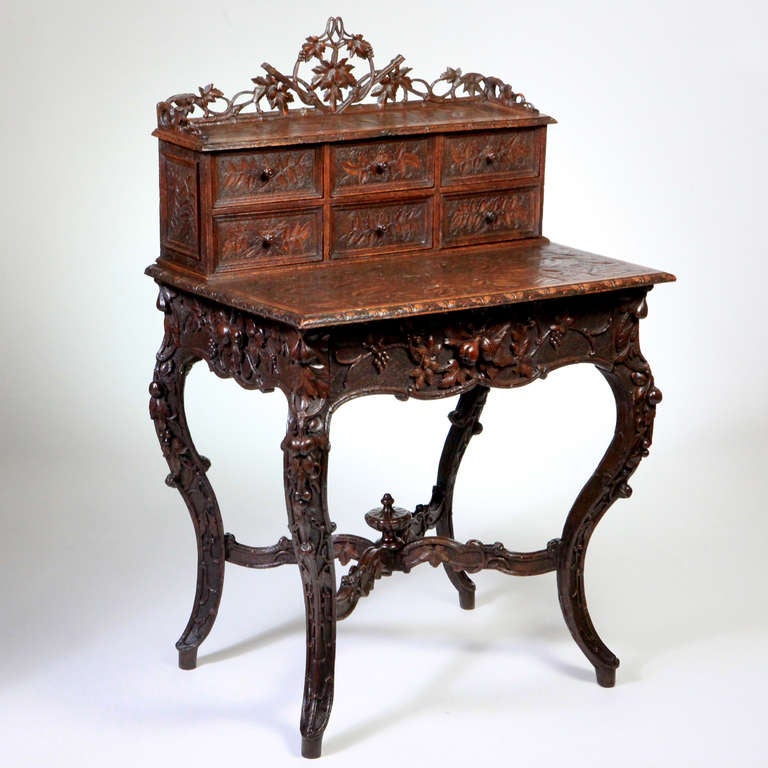 Rare carved black forest ladies writing desk. The top gallery with a carved leaf pattern and six small drawers. Apron front opens to large centre drawer. All seven drawers meticulously re-upholstered in deep green satin with rope trim. Carved leaf