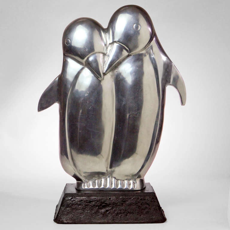 Large penguin sculpture with two polished aluminum metal birds raised on a base.