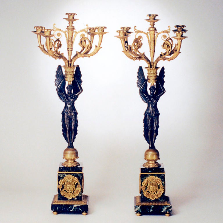 Important pair of French Empire-style five-light bronze candelabra. Each richly patinated winged victory figure rests on a serpentine base with gilt bronze mounts and holds an elaborate gilt bronze candelabrum.