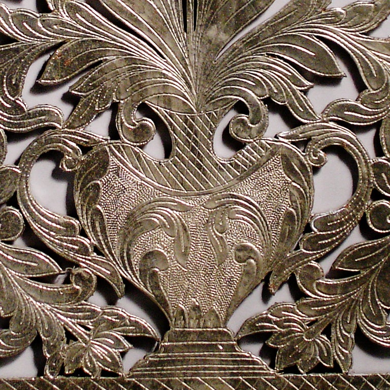 Striking silver wall hanging.  Intricately carved in wood with silver-wash painted finish.  Vase motif with flowers and leaves and beveled frame with lattice detailing.
