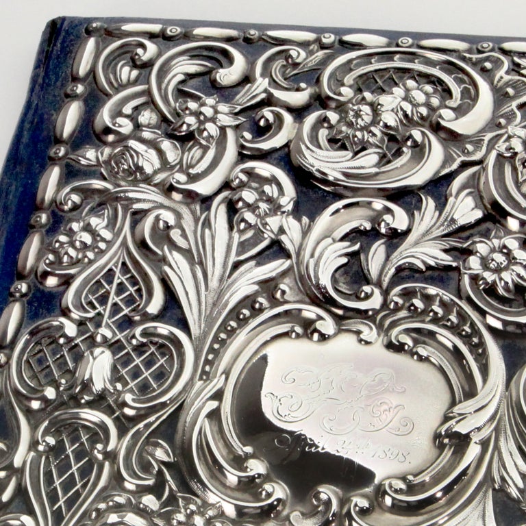 Rare preserved Victorian WILLIAM COMYNS silver and leather desk blotter.  Navy blue leather folder with interior covered in matching blue silk moire, including inside envelope pocket.  Finely detailed sterling silver overlay in magnificent scroll