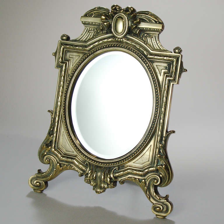 Victorian standing vanity mirror. Sculpted brass design with scrolled and beaded decoration framing beveled oval mirror.