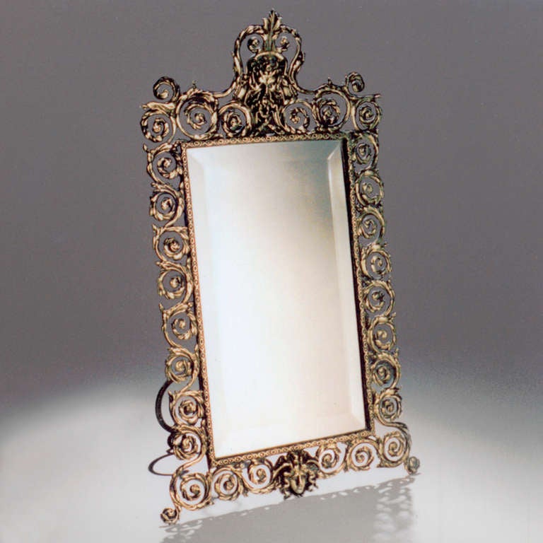 Brass table or vanity mirror with scrollwork and detailed female masks on top crown piece and bottom.