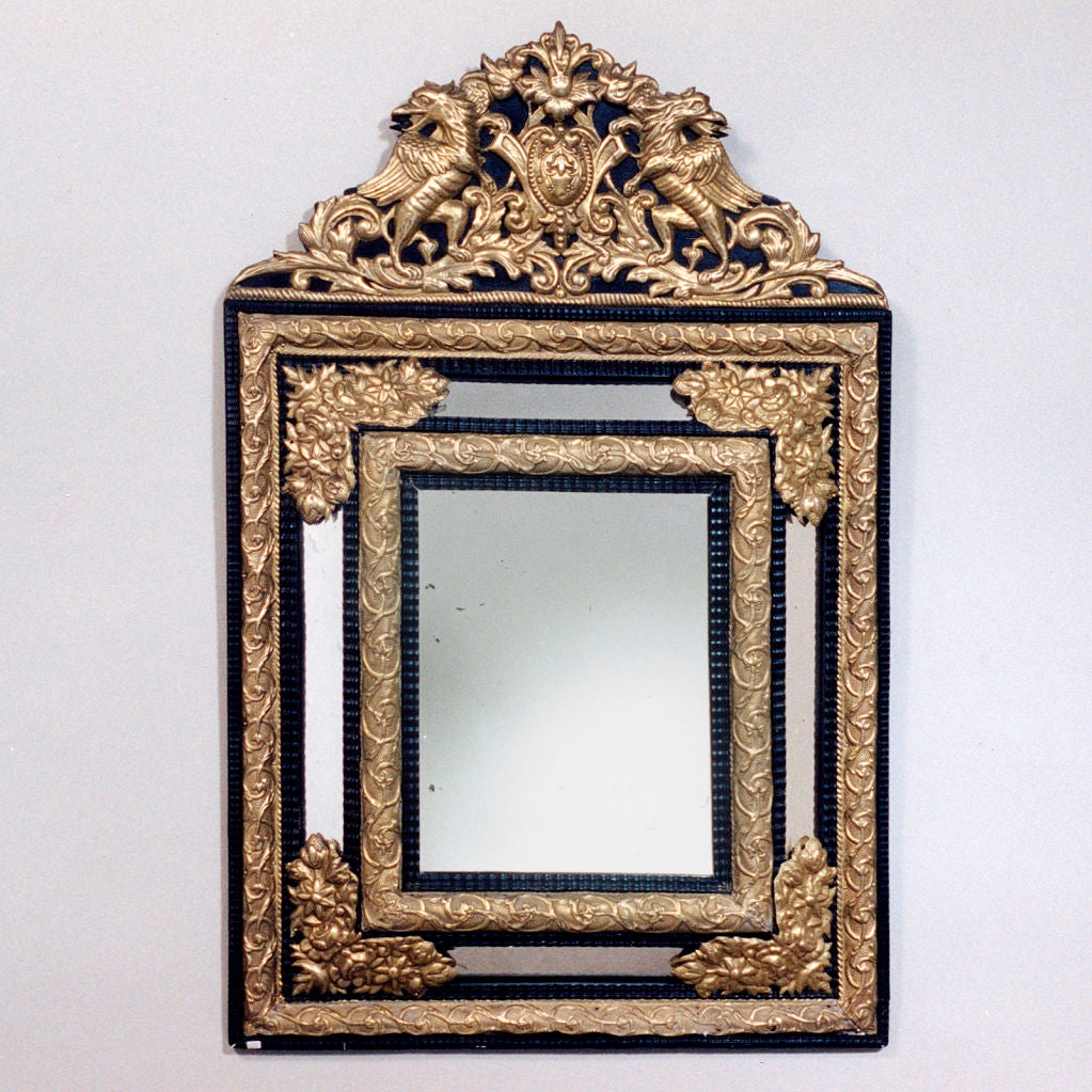Elegant Napoleon III style brass and ebonized wood cushion mirror. The arched top has winged griffins flanking a crest. The mirror mounts with fine detailed floral pattern overlay in brass.