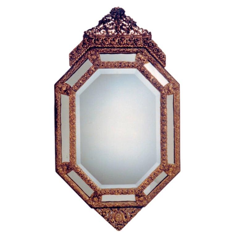 Octagonal cushion mirror with ornate brass repousse frame and triangular crown, apron with floral motifs.
