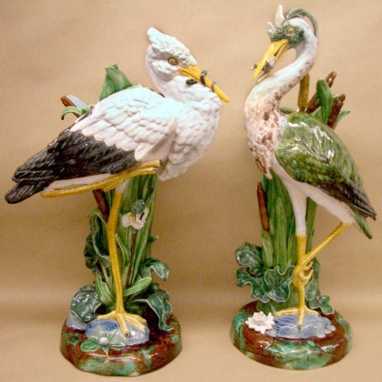 Rare matched pair of English Majolica flower vases by Joseph Holdcroft. Each figure with a tall cattail vase; the gray and white heron with fish in his mouth, the companion white stork with an eel in his mouth. Each perched on a natural rocky mound.