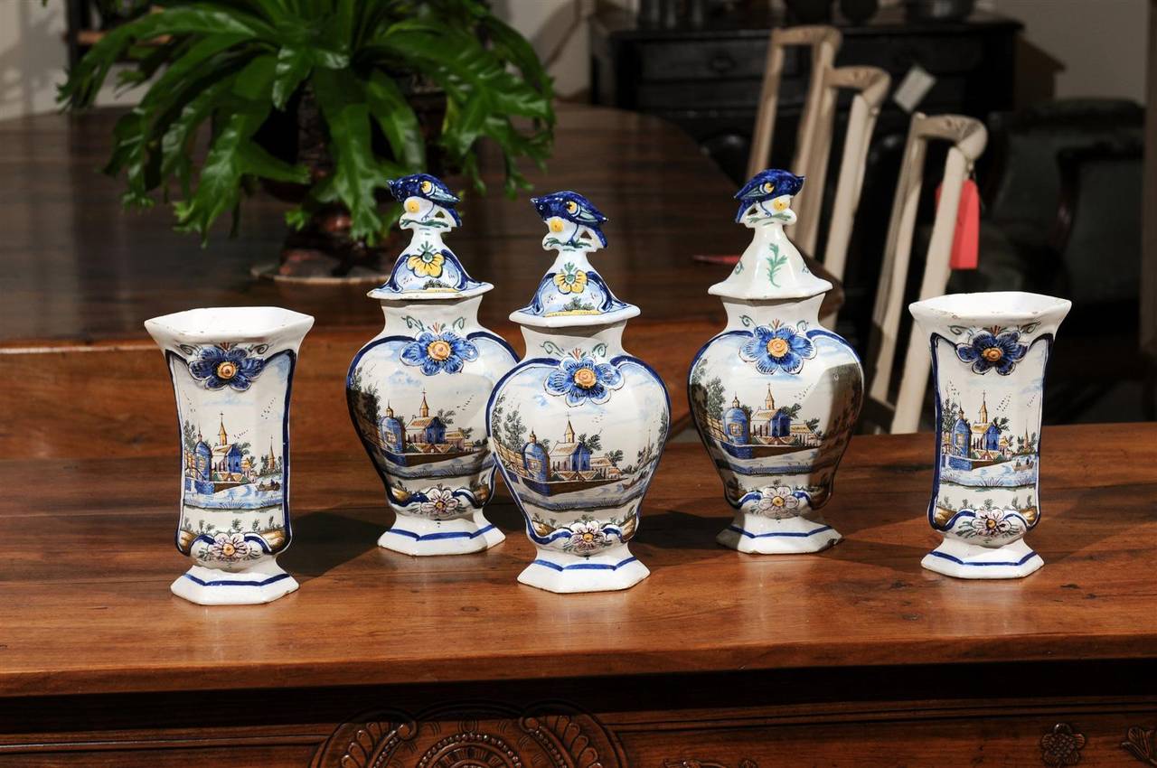 19th Century Delft Garniture Set, Circa 1890
This charming five piece garniture set has been painted in blue and yellow.  The bucolic scene of two fishermen floating in front of their town with the church spire in the background has been repeated on