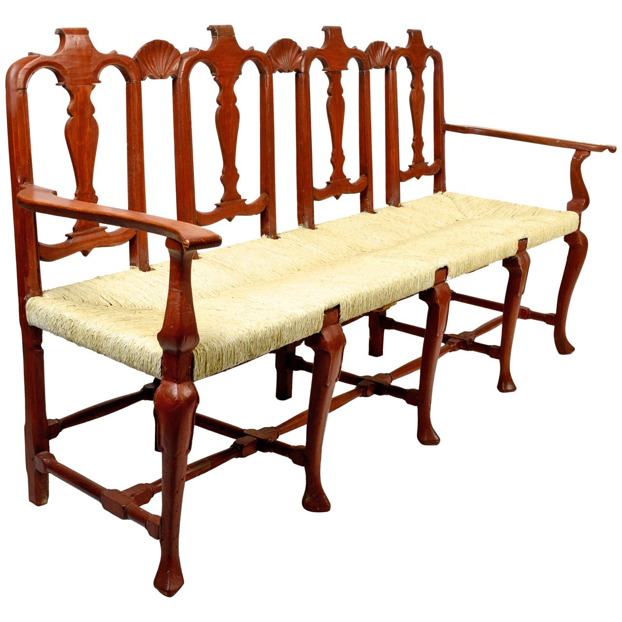 This unusual rush seated bench has four beautifully carved backs connected with three carved shells. It stands on five cabriole legs with trifid feet. It has a red washed finish and a painted rush seat. A great piece for a sizable entry or