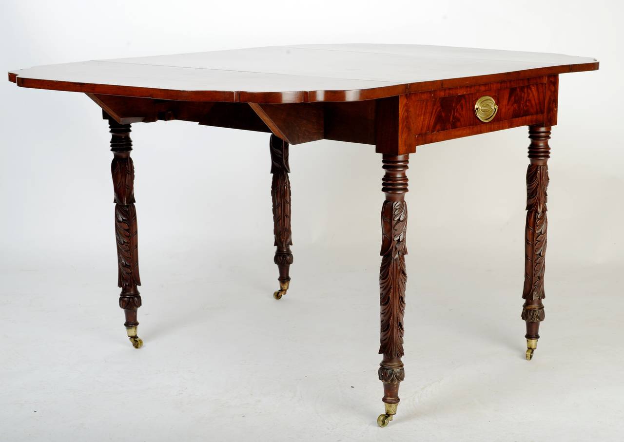 This handsome American table has beautifully shaped drop leaves and legs with beautifully carved acanthus leaves. It has a single drawer with an original brass pull and brass casters. An exquisite American piece for any style of décor. Table opens
