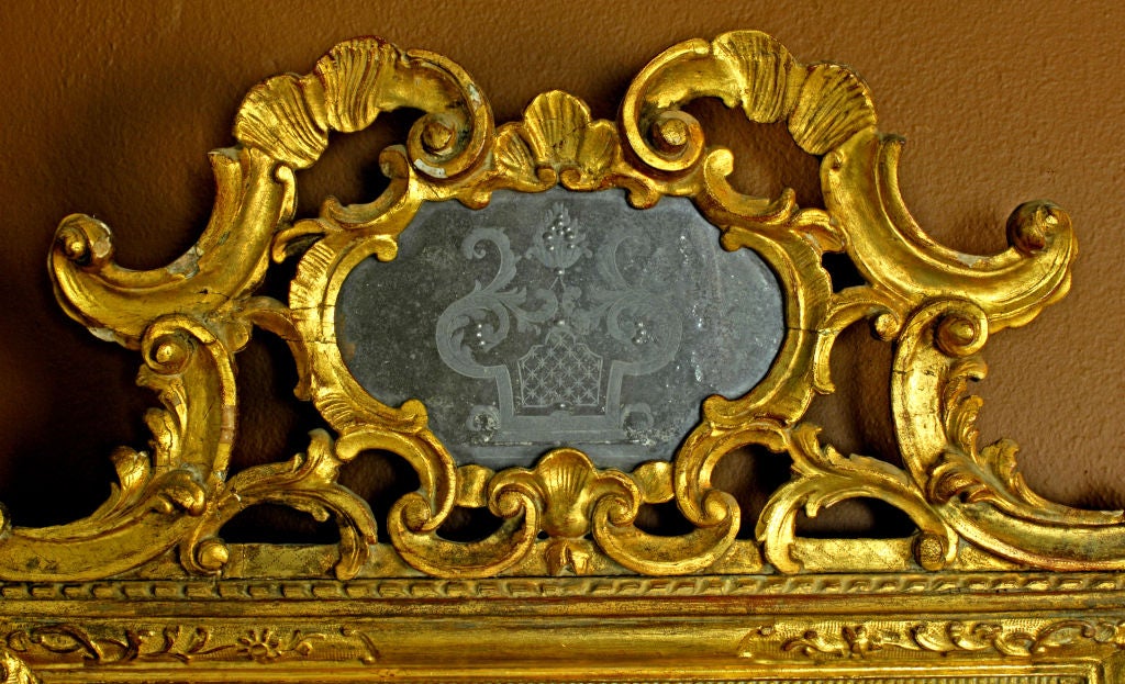 Venetian gilt carved mirror, c1750. Surmounting the larger mirror is a smaller, cartouche shaped reverse etched mirror with pierced cresting, C-scrolls and foliate sprays. The surface is giltwood and it retains its original mirror plate.
N.P. Trent