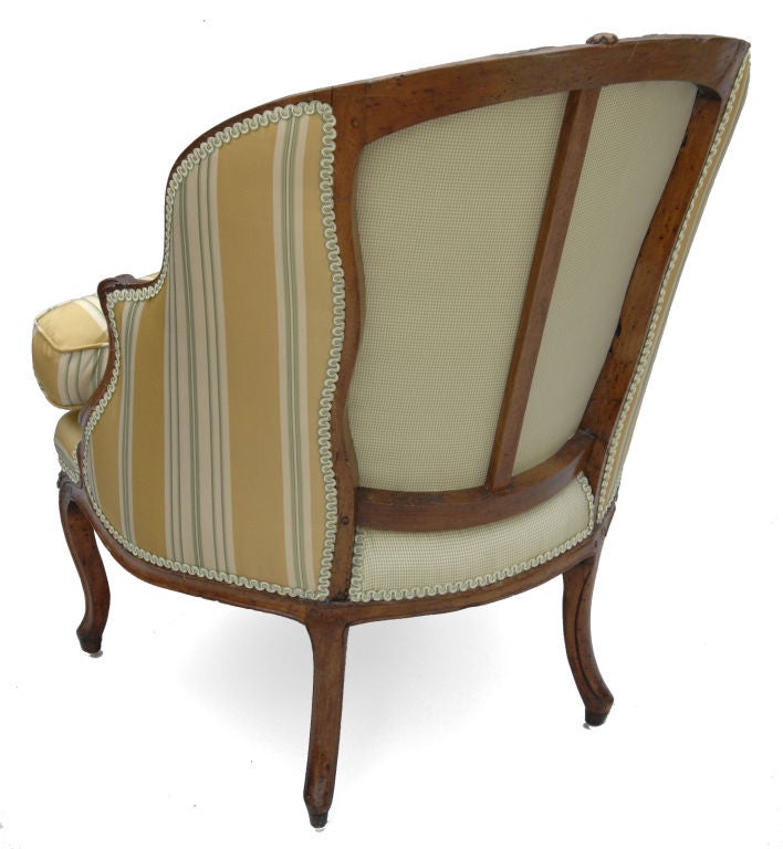 This French bergere has the typical carved details of Louis XV period. A carved rose motif appears at the center of the crest rail, on the stretcher and on the cabriolet legs. The beautiful curved back displays the traditional open back support. A