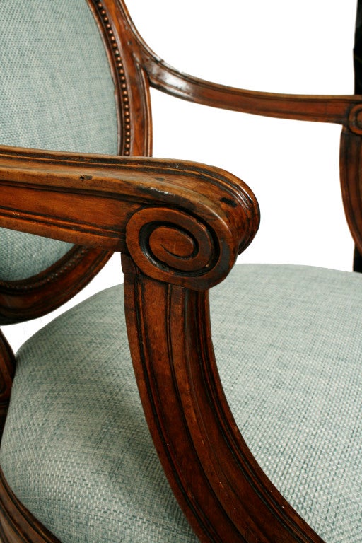 This beautiful pair of neoclassical walnut armchairs have medallion shaped backs with a border of carved beads. The C-scrolled arms sit on down swept supports. The bow fronted seats are raised on tapered legs that have gadrooned collars and ball