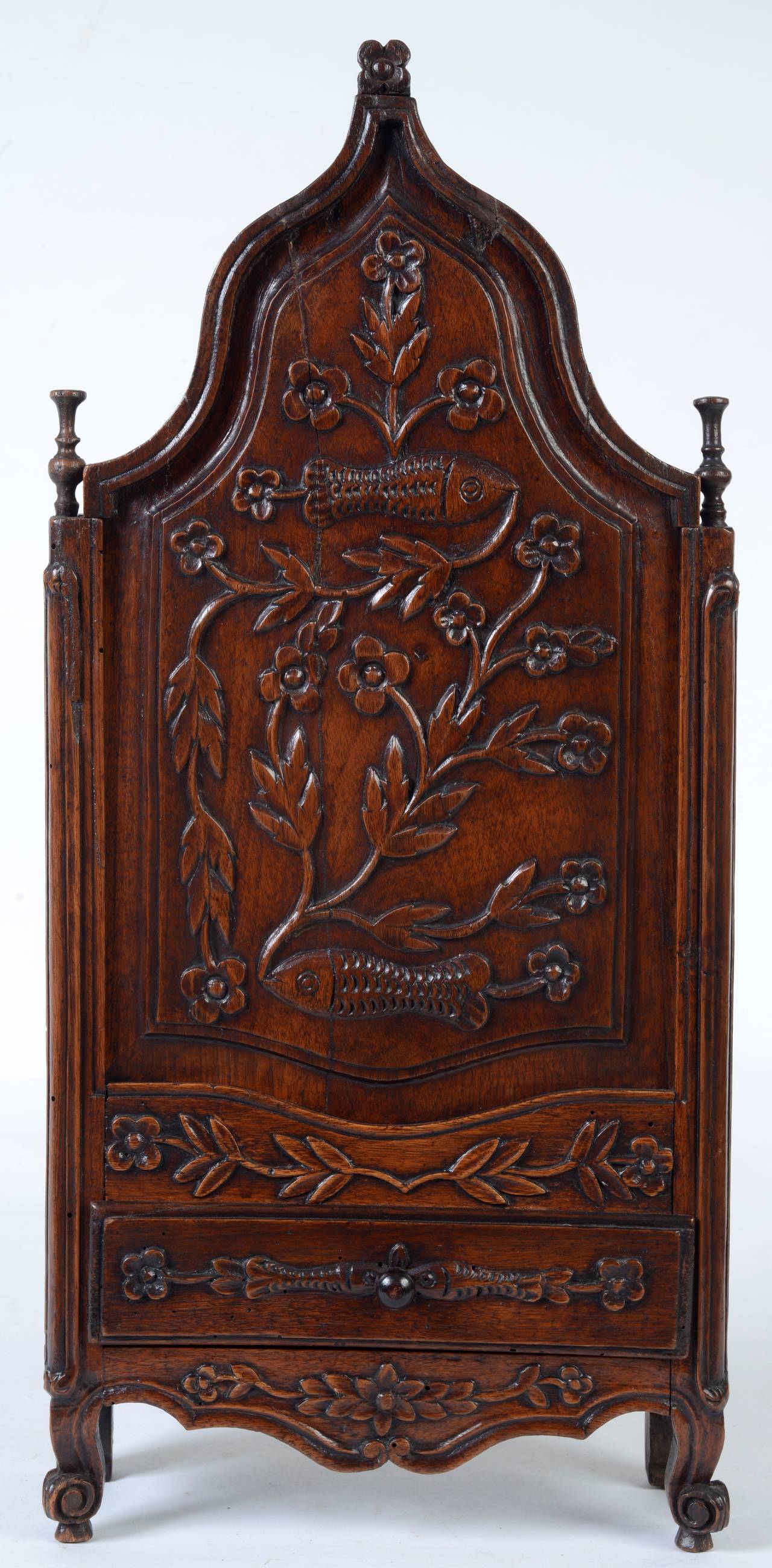 This fine French candlebox is made of hand-carved walnut. The sliding front panel is carved with stylized flowers and fish. It has a single drawer also carved with fish and flowers. It stands on cabriole legs with escargot carved feet and is topped