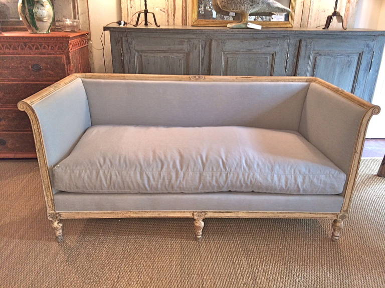 Handsome cream painted small settee from the French Empire period. Newly upholstered frame up in a pale sterling blue Irish linen. Expected wear to expose the frame.