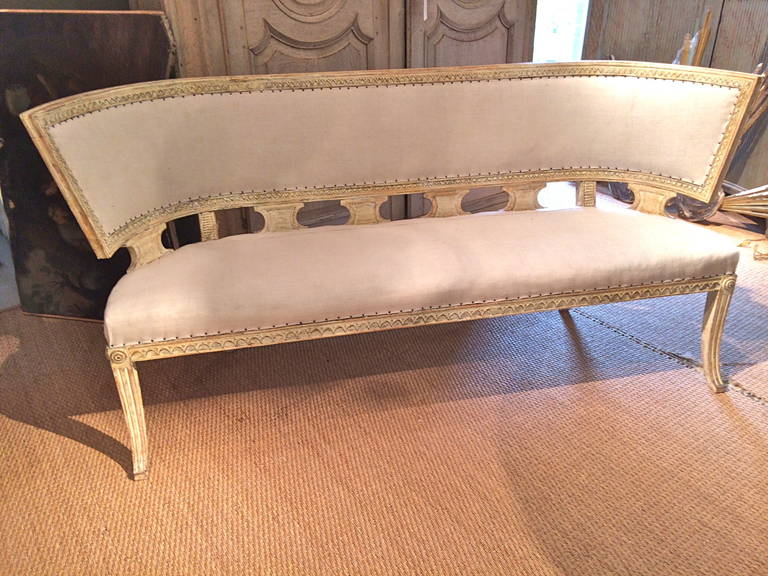 Handsome and unusual Swedish Gustavian settee in the form of a Klismos. Scraped to original off-white paint. Beautifully carved. Saber legs front and back. Upholstered in rough white antique linen.