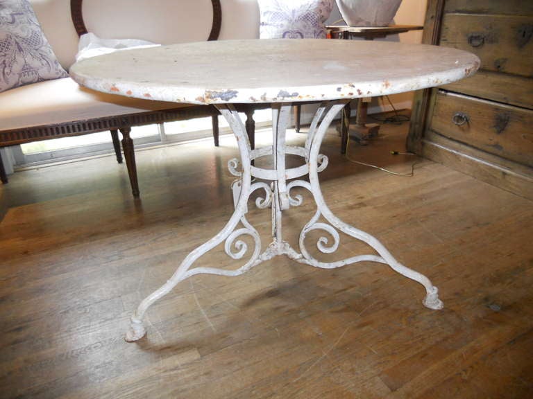 Unusually large French Iron garden table manufactured at Arras. Beautifully scrolled and curly iron base with hoof foot. Crusty white paint. Numerous paint chips on edge of top.