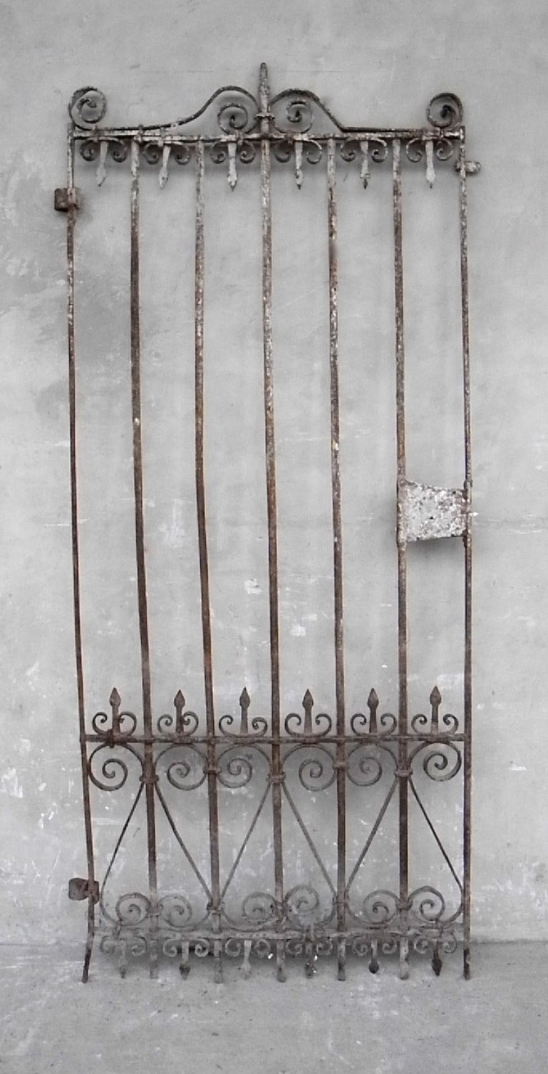 This small, antique iron gate features intricate iron-work along the top and bottom edges. Perfect for the entrance to a small garden, this piece sports an elegant and rustic patina.