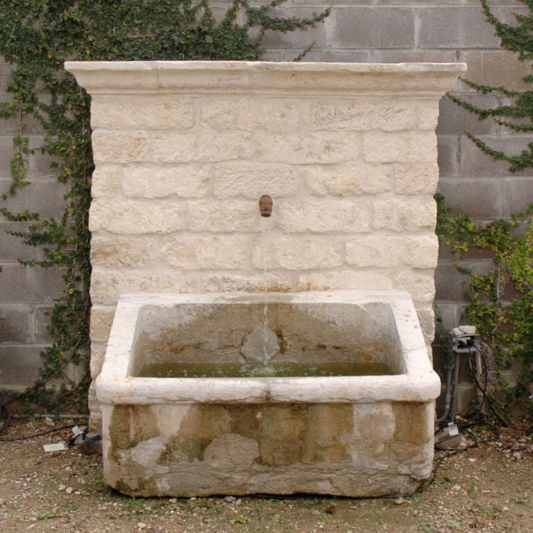 This 18th century stone wall fountain originally graced the courtyard of a Mas near the Provencal town of St. Remy. This monumental piece consists of a stone auge basin, a buget wall, and a 19th century iron spout. The basin is 10