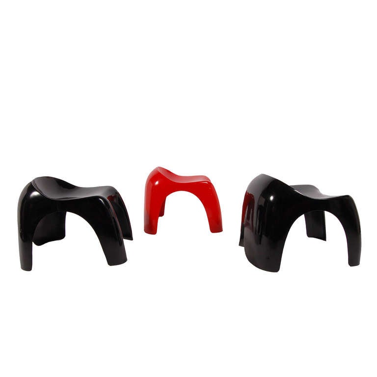 Two black and one red stackable molded plastic, injection molded ABS resin stools. These are the larger version; a smaller children's model, Efebino, was also produced. Low back, seat scooped out in general form of tractor seat. Rounded cornered