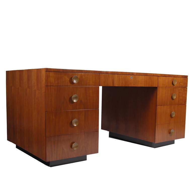 Desk with two banks of drawers, one file drawer. Walnut with solid brass disc handles. On black painted bases. Made by Herman Miller.