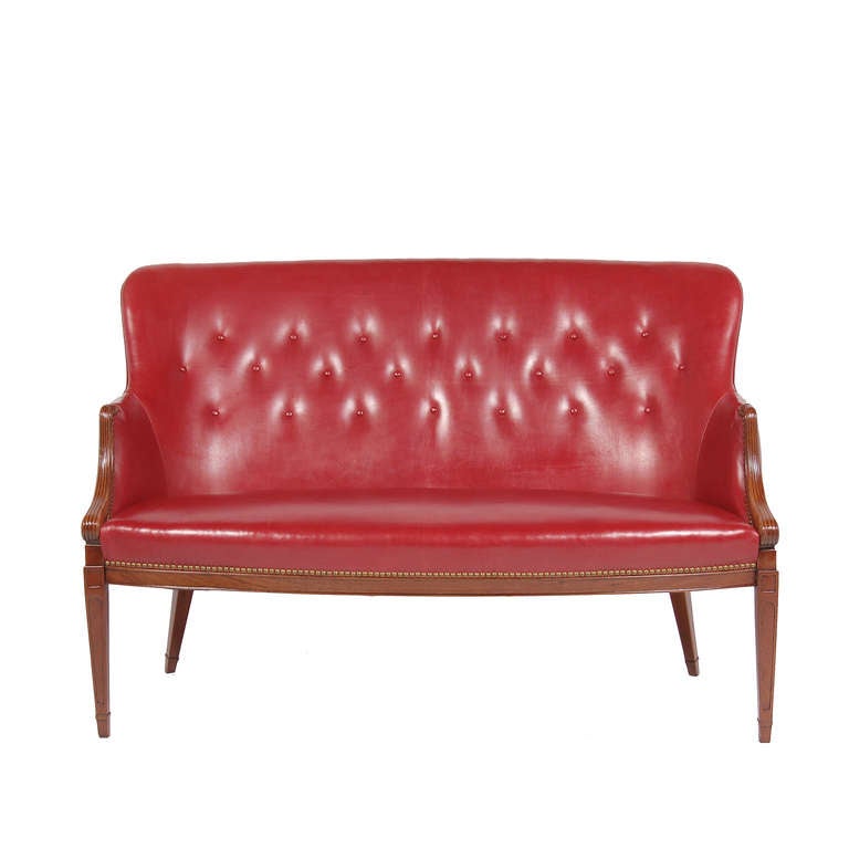 Neoclassical two-seat sofa, solid mahogany frame with sculpted arms and cathedral legs. Reupholstered in new red leather; brass nailhead trim and tufted back.