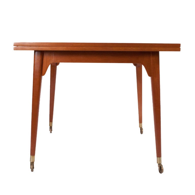 flip-top table, mahogany top on solid mahogany legs with brass feet on casters. Top pivots and unfolds. Extends to 68