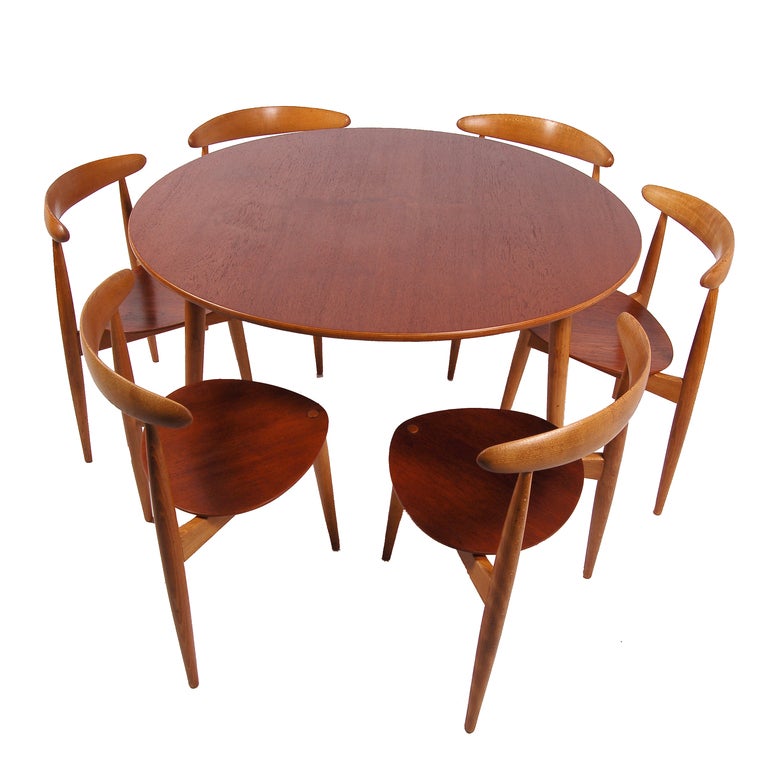 Round dining table with three legs, teak with beechwood base. Six three leg chairs that fit in two per section, beechwood with teak seats. Marked with FH (Fritz Hansen) and distributor's label, Raymor.
