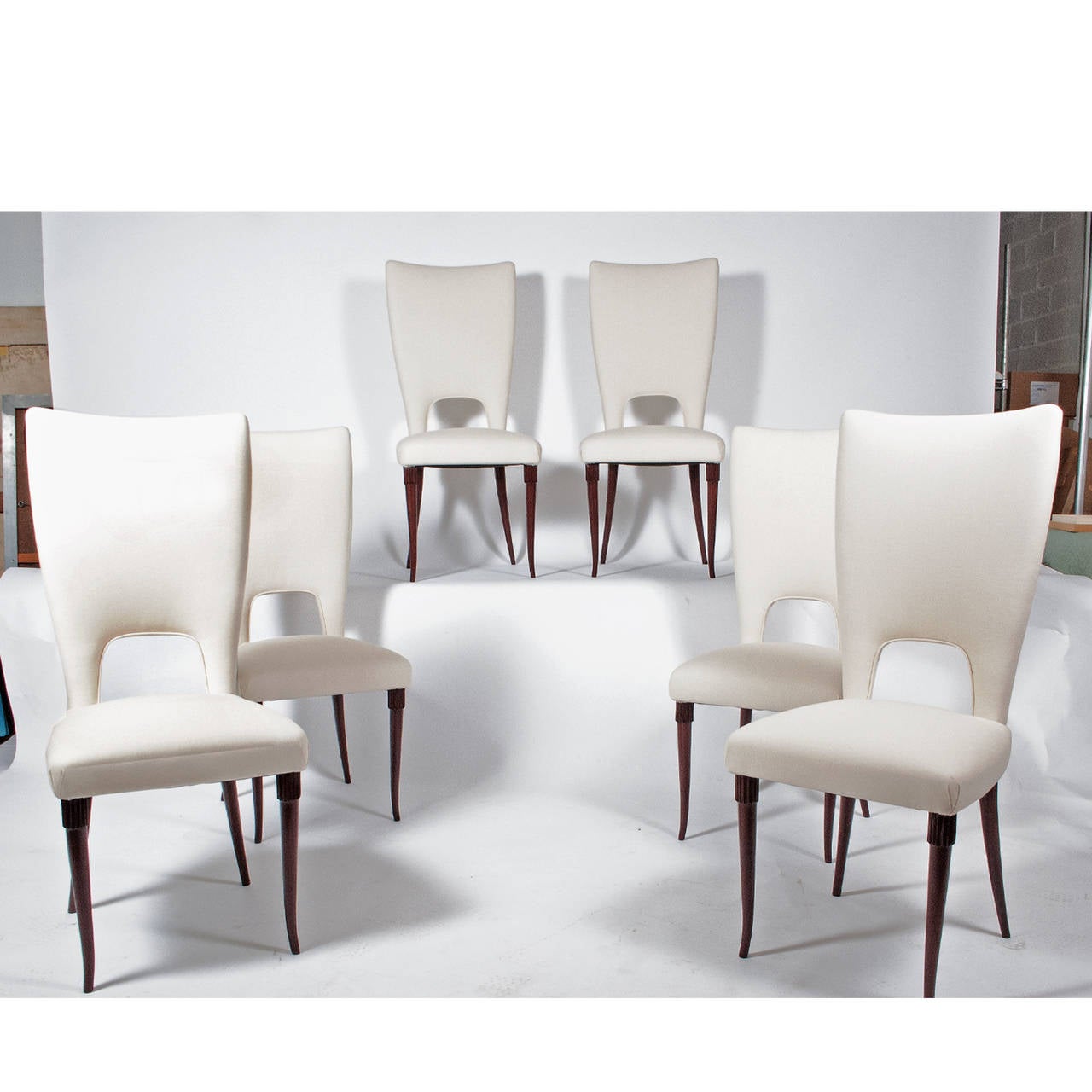Sensuous high back chairs with opening at back, fully upholstered on curving, hand-sculpted wood legs with fluted detail. Retains label, 