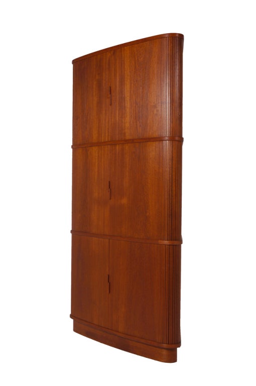 Elegant corner cabinet with rounded edges, three tambour doors and interior shelving and drawers. Teak with birch interior. Made by J.L. Moller.